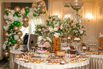large group of different desserts arranged on event with decorations, balloons and flowers in luxury restaurant.