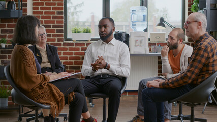 African american man making confession about addiction and rehabilitation with people at group therapy. AA meeting with patients talking about alcoholism and progress in circle.