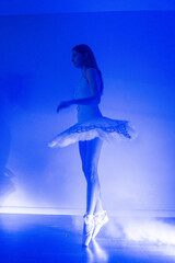 Ballerina with long legs posing in blue light