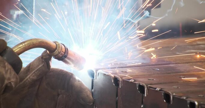 Closeup craftsman male hands protective gloves working with welding machine surrounded by illuminated spark blur bokeh. Man welder manual engineering industry connect metal part with heat temperature