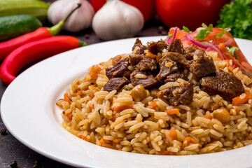 pilaf with beef and vegettables salad on white plate on dark table macro close up