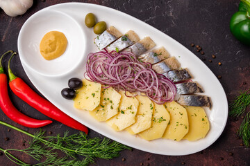 Herring with potatoes and red onion on white plate top view