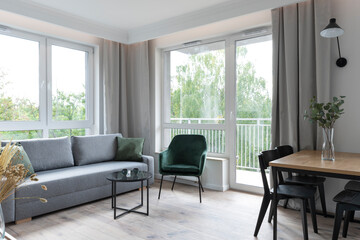 Interior of living room with big window, comfortable sofa, armchair and wooden floor. Scandinavian architecture in cozy room .