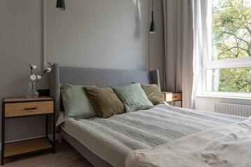 Cozy bedroom in apartment with window, bed with pillows and blanket. Stylish room in hotel for sleep. Wooden furniture in new apartment.