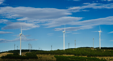 Panoramic view of modern windmills installed on the hills of the countryside amidst the vegetation....