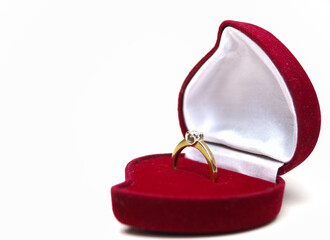 Beautiful shiny gold ring with a large diamond of high quality. In a red velvet box in the shape of a heart. Red background. Copy space.