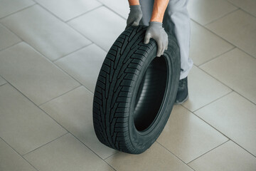 Changing tires season. Man in uniform is working in the autosalon at daytime