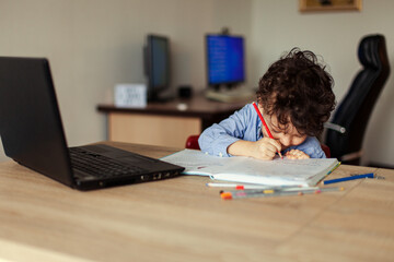 A preschooler learns online at the computer and writes an assignment in a notebook at home.