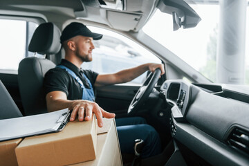 Modern vehicle. Delivery man in uniform is indoors with car and with order