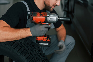 Using equipment. Man in uniform is working in the autosalon at daytime