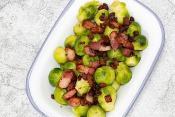 Brussels sprouts with bacon lardons in a traditional enamel dish.  On a concrete background