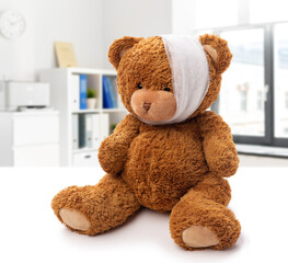 medicine, healthcare and childhood concept - teddy bear toy with bandaged head having toothache over medical office at hospital background