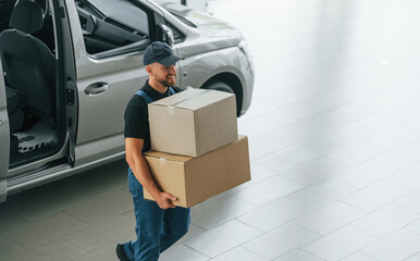 Business of service. Delivery man in uniform is indoors with car and with order