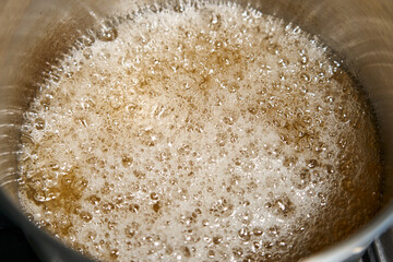 bubbling and boiling liquid with bubbles in a brown saucepan