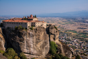 Fototapeta na wymiar Beautiful scenic view of Orthodox Monastery of Áyios Stéfanos (St. Stephen) on cliff, immense monolithic pillar, at the background of stone wall and rock formations of Meteora mountain, Greece.