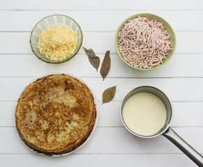 Foodstuffs for lasagna on a white wooden background.