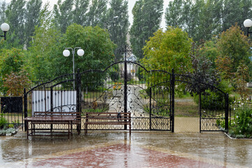 Heavy downpour in park. Wrought iron gates and two benches