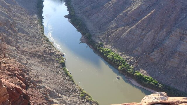 The Colorado River, Seen From An Overlook In The Maze District Of Canyonlands National Park In Utah. A Group Of People On A Rafting Trip Are Seen Camped On The Sandy Riverside.