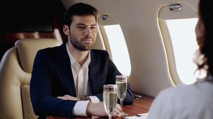 Smiling businessman looking at girlfriend near glasses of champagne in private plane.