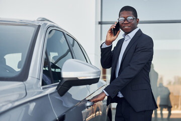 Young african american businessman in black suit is near automobile outdoors