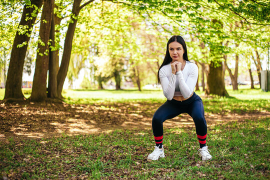 Girl stretches, prepares her body and muscles for a productive fitness workout. Flexible female sporty model in the city park. Image with copy space.