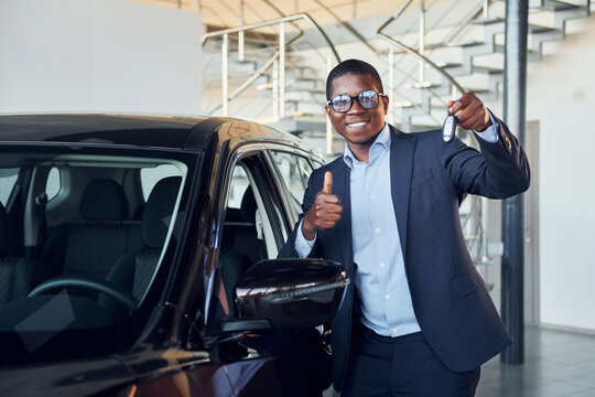 Holding keys in hands. Young african american businessman in black suit is the autosalon