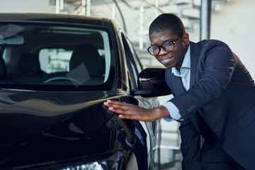 Young african american businessman in black suit is the autosalon