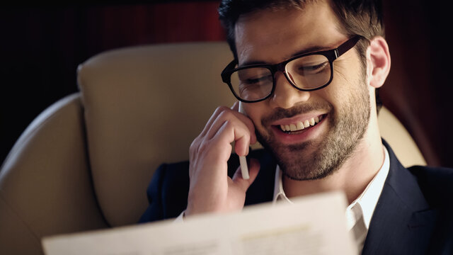 Smiling businessman talking on cellphone and reading newspaper in private jet. - Powered by Adobe