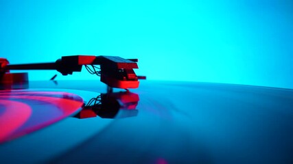 Black vinyl record spinning and play music on old turntable in rays of bright red and blue neon lights. Turntable needle on vinyl record, reads recording from grooves on disc. Close up. Slow motion.