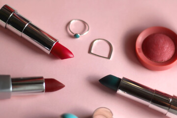 Various lipsticks, pink blush and silver rings on bright pink background. Selective focus.