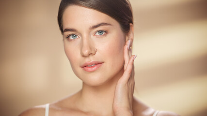 Female Beauty Portrait. Happy Caucasian Woman with Brown Hair and Light Green Eyes Posing, Touching Her Natural, Healthy Skin. Wellness and Skincare Concept on Warm Isolated Background. Close Up.