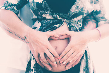 Man and Pregnant Woman holding their hands in a heart shape on her baby bump. Pregnant Belly with fingers Heart symbol. Maternity concept.
