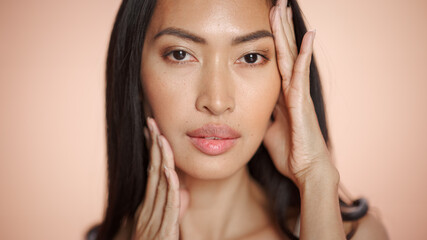 Obraz premium Female Beauty Portrait. Beautiful Asian Brunette Woman Posing, Smiling, Touching Her Face with Natural, Healthy Skin. Wellness and Skincare Concept on Soft Isolated Background. Close Up.