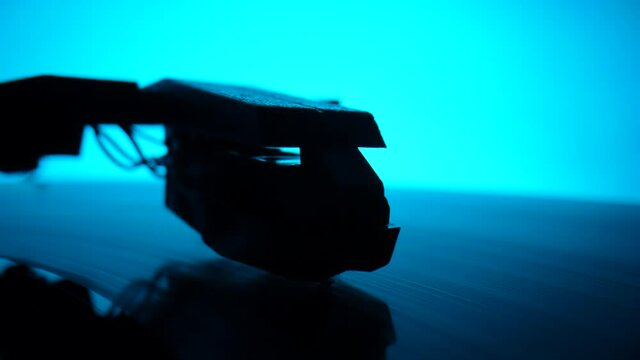 Music retro turntable with spinning vinyl record against backdrop of blue lights. Camera focuses on the turntable needle on vinyl record, then moves away and the picture becomes blurry. Slow motion.