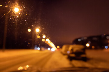 Night winter city street with lights, blurred view through car windshield
