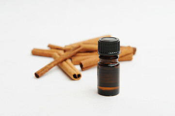 Small dark glass bottle in front of cinnamon sticks on white. Essential oil or extract. Cosmetic or food concept
