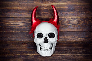 Human skull with red fabric horns on brown plank background