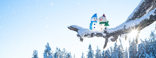 Winter snow snowman background panoramic banner panorama - Little cute Snowmen sits on branch of tree in snow snowy black forest with snowflakes and sunshine..
