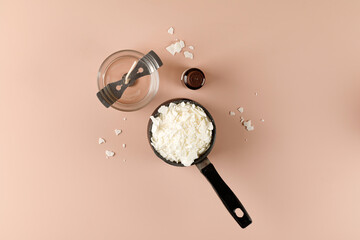 Equipment for candle making with white soy wax flakes, fragrance and jar with wick. Flatlay, top view. Peach background