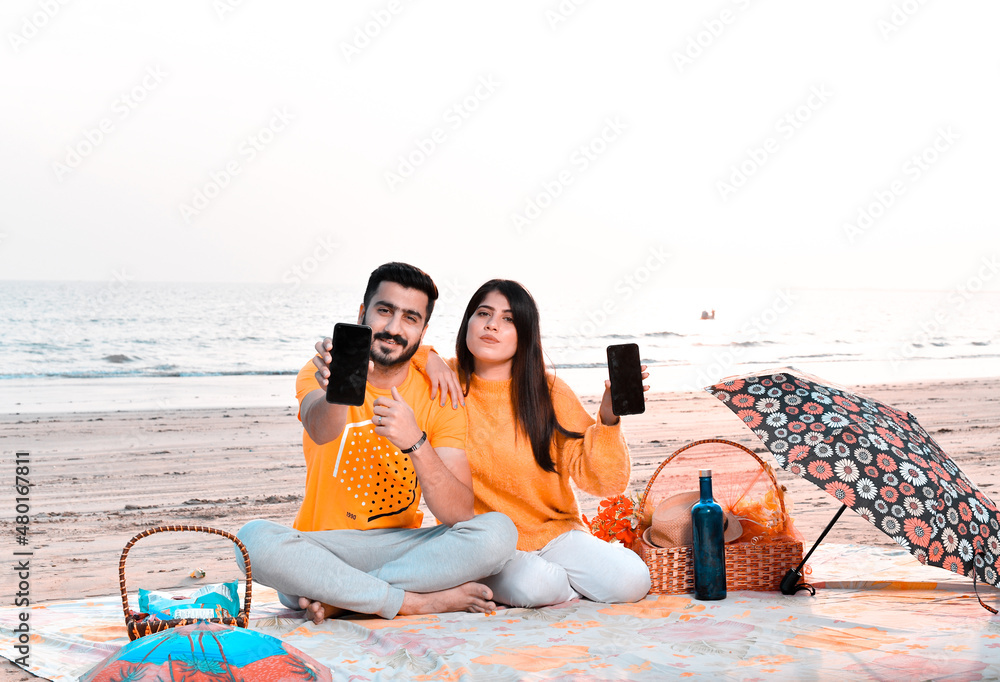 Wall mural casual happy couple showing cellphone on beach indian pakistani model