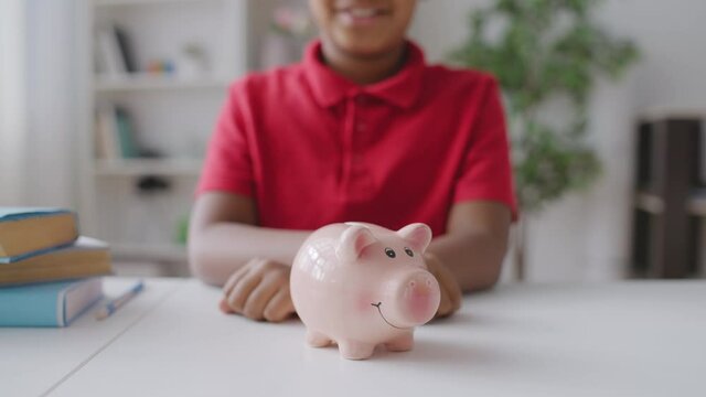 School kid saving money, putting coin in piggybank on the table, financial plan