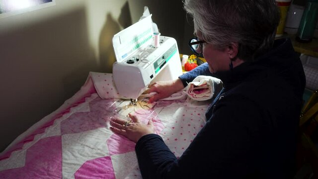 Senior woman using a sewing machine to stitch a pattern on a handmade quilt