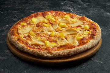 Pizza with chicken and pineapple on a black stone background. 45 degree angle view. Close-up, selective focus