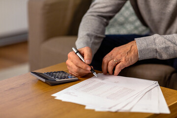 savings, annuity insurance and people concept - close up of senior man with papers or bills and calculator writing at home in evening