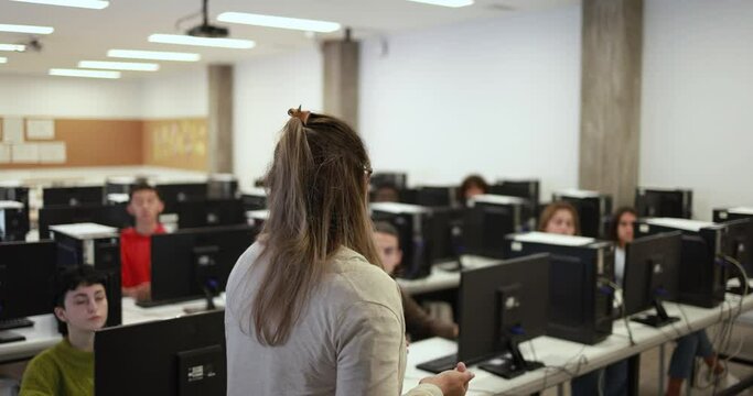 Mature teacher working with multiracial students inside computer classroom at school