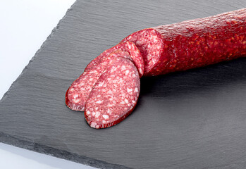 A stick of smoked sausage and slices of sausage on a black cutting board