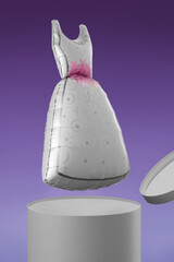 Shot of a balloon shaped as a pretty gray dress with pink flowers. The silver balloon is flying out of a gray box. The photo is taken on a violet background.