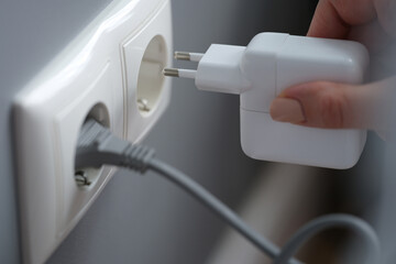 Female fingers plug the power adapter into an outlet
