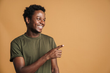 Young black man wearing t-shirt smiling and pointing finger aside