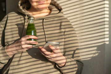 woman holding a phone and glass bottles with juices